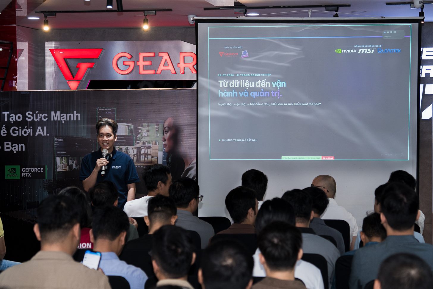 Ảnh chụp mình cầm mic mở màn trên sàn showroom GearVN, phía sau là màn chiếu tiêu đề buổi workshop